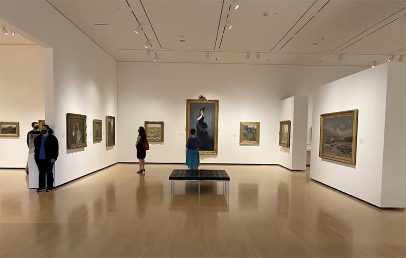 3 people stand, observing medium and large paintings in a gallery with white walls