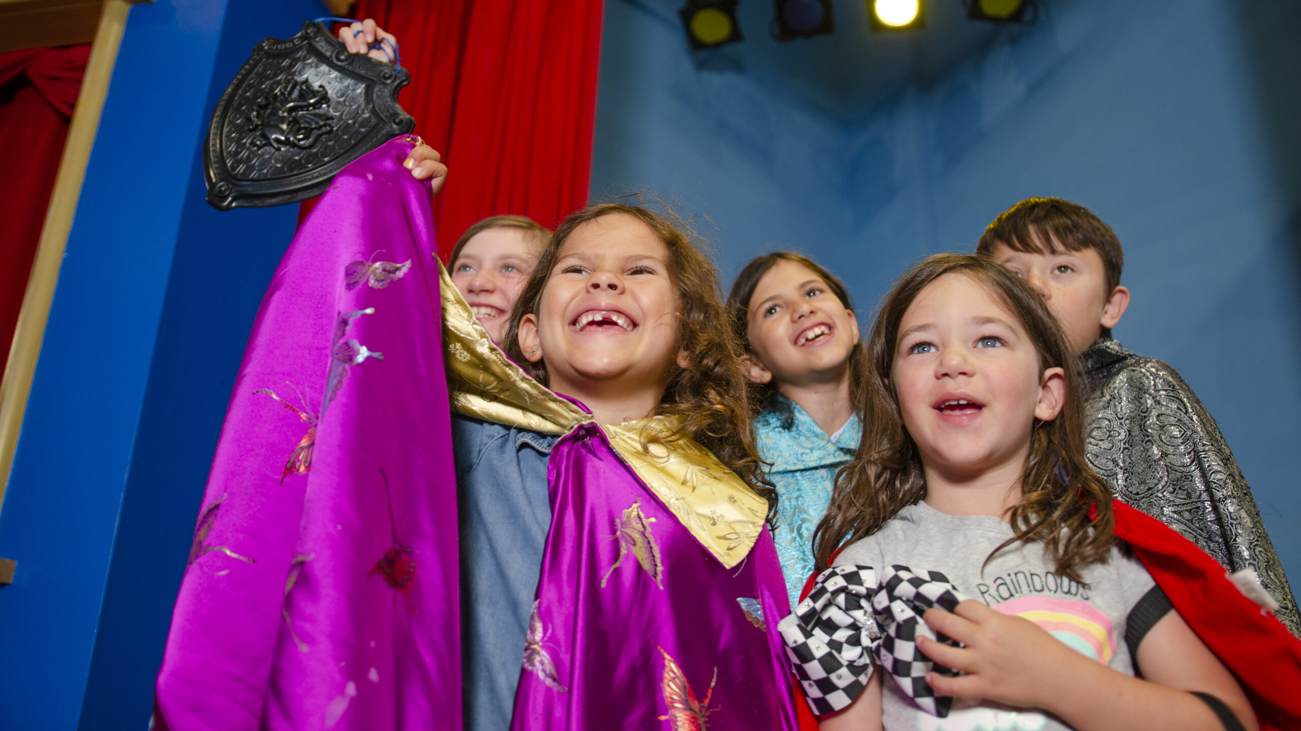 a group of young children, dressed in costumes, excitedly pose in the theater space of Art Venture