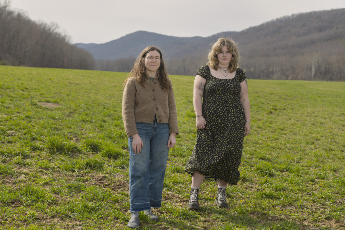 Photo of 2 people standing in a field with a backdrop of mountains behind them