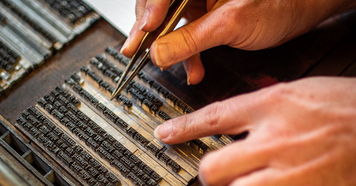 A pair of hands setting letters in a letterpress