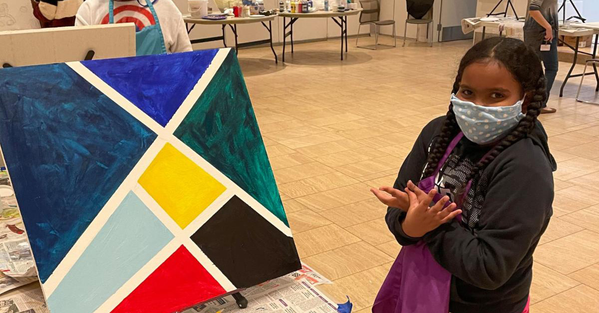 A child in a mask standing next to a painted ceiling tile