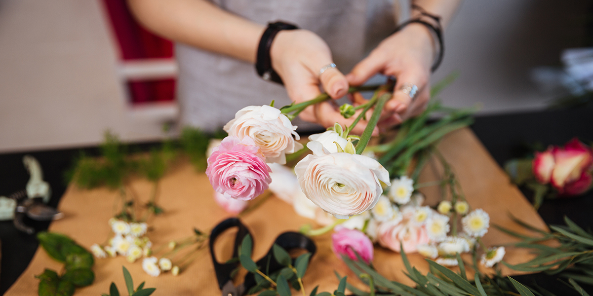 Closeup of hands of young woman florist creating bouquet of pink roses on the table
