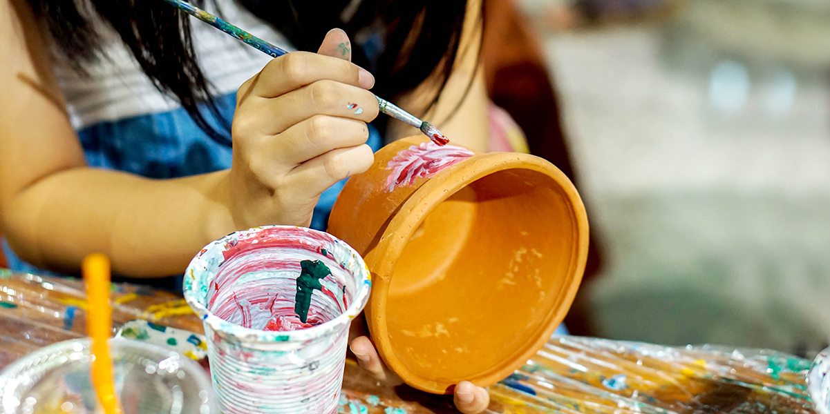 A person holding a terracotta pot while painting it with a small brush