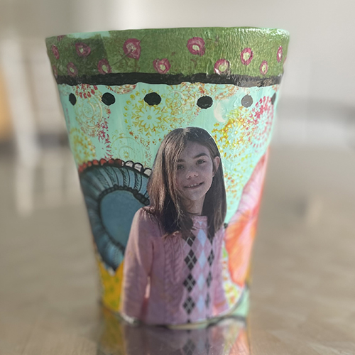 A small flowerpot decorated with painted swirls and a photo collage of a little girl