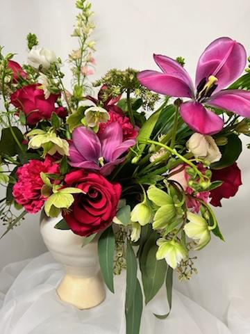 A floral arrangement featuring pink and red flowers and greenery in a white ceramic vase