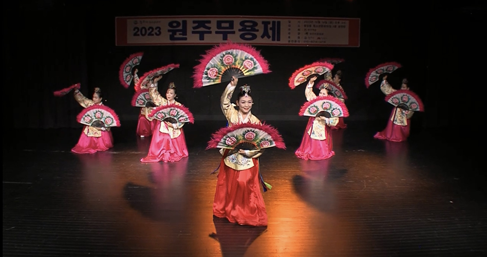 A group of women dressed in traditional Korean clothing performing a fan dance