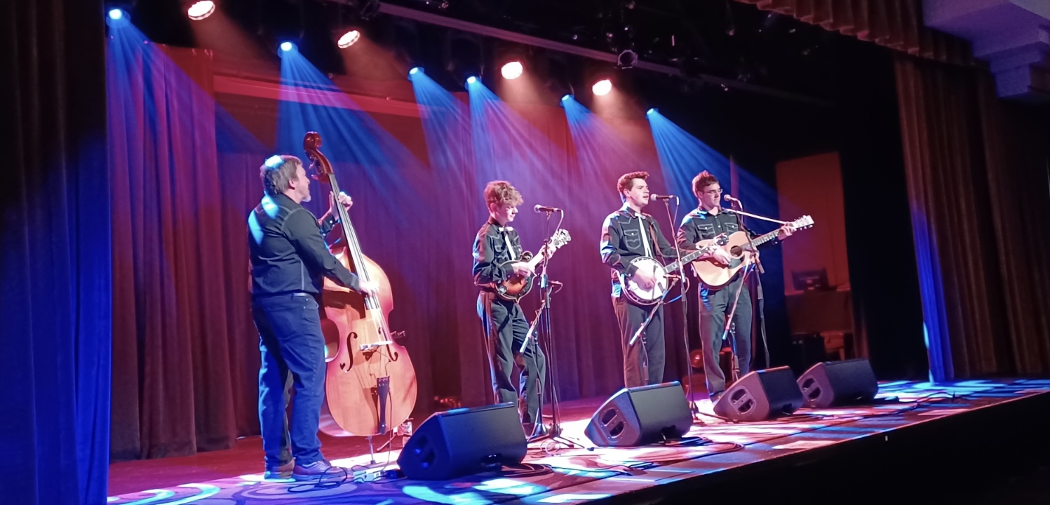Four young men perform music on a brightly lit stage