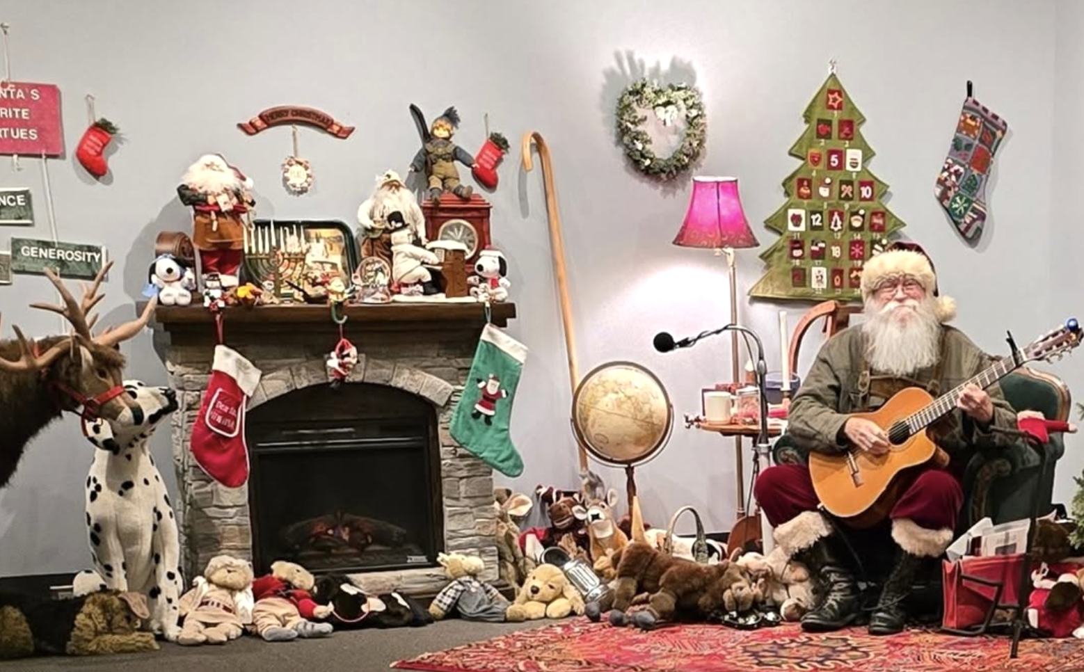 Santa holding a guitar while sitting in a chair in his workshop featuring decorations and a fireplace