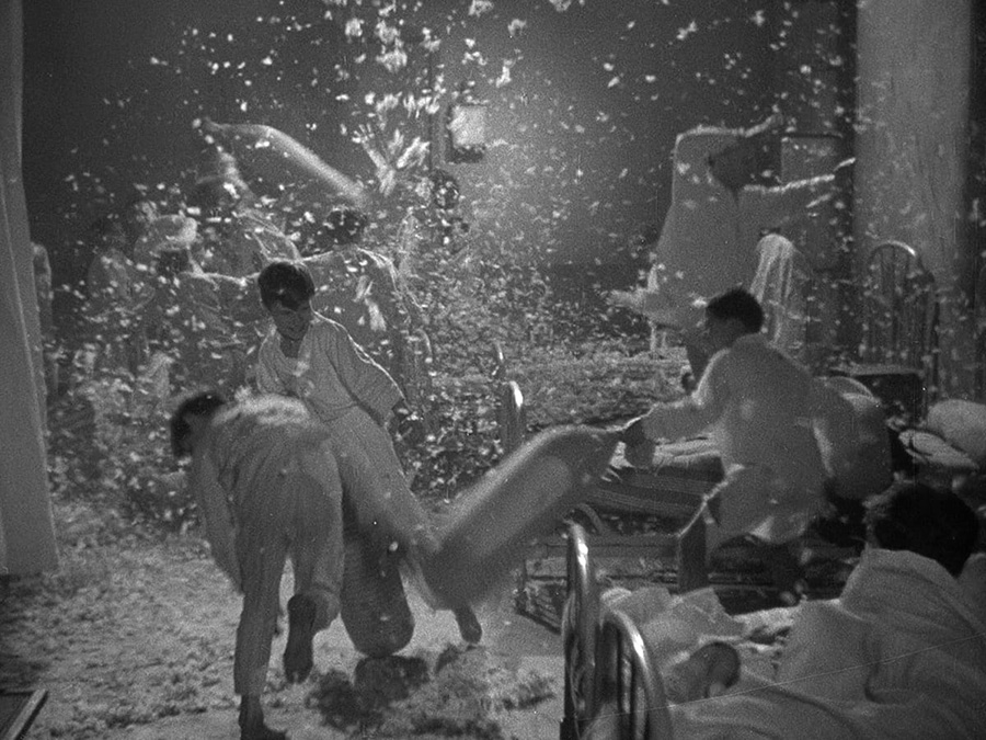 Black and white film still of boys in pajamas holding a pillow fight with feathers flying all around them