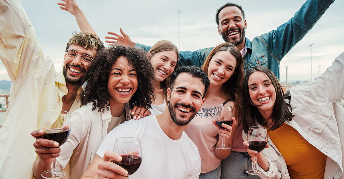 Group of young adult best friends having fun toasting a red wine glasses at rooftop reunion or birthday party, drinking alcohol. Happy people enjoying on a social gathering celebrating together