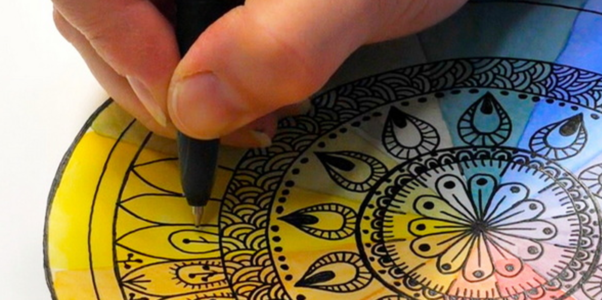 A close up shot of a person holding a pen as they color in a multicolored mandala