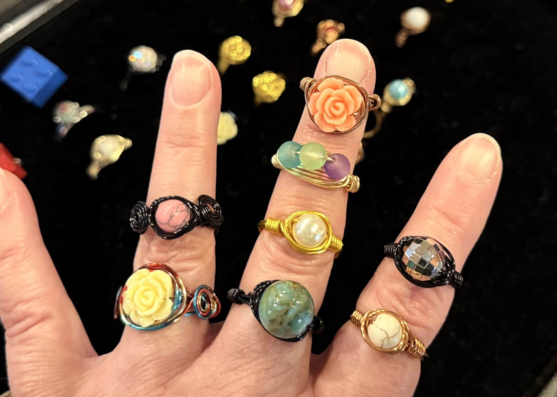 A hand displays 8 different wire-wrapped rings that feature various beads and stones