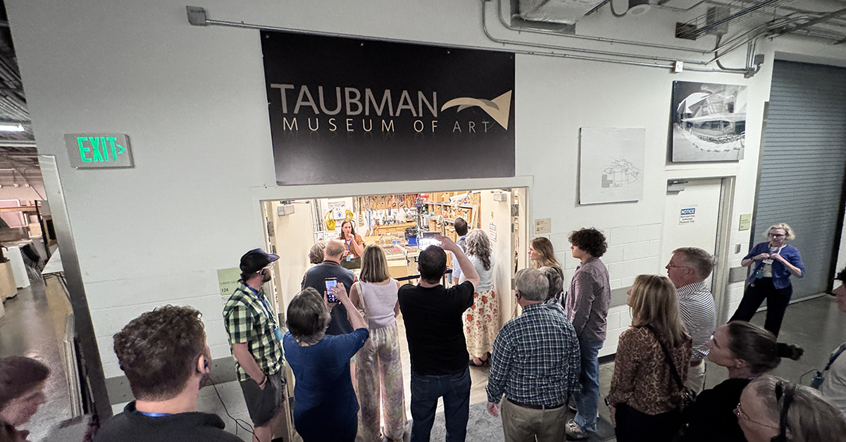 A tour group listens to a guide describe the wood workshop inside of a museum