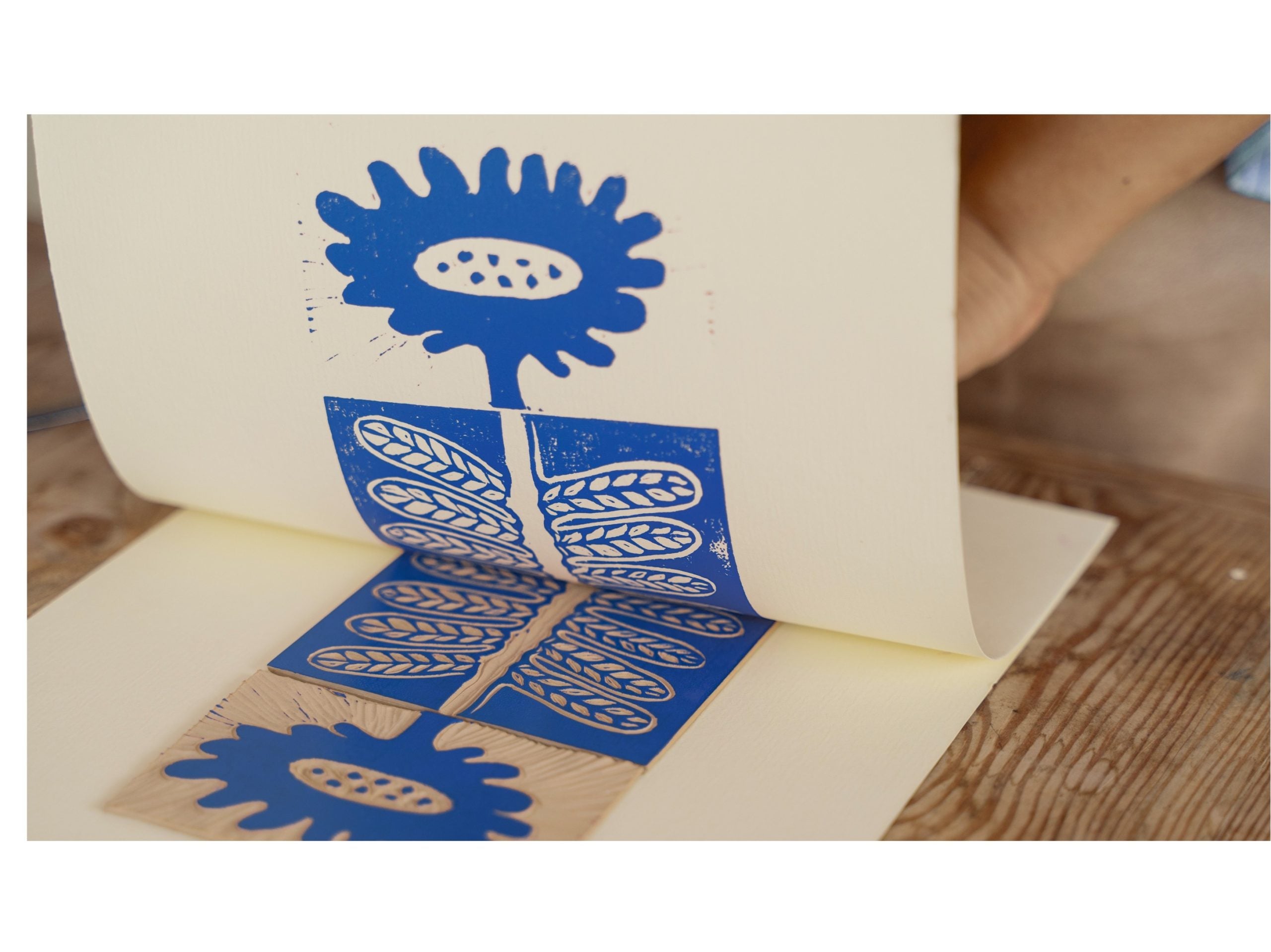 Image shows a hand lifting a print of a blue flower from the printblock